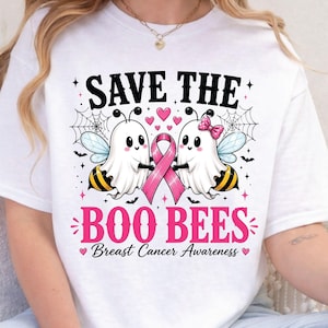 May include: A white t-shirt featuring a graphic of two ghost bees holding a pink breast cancer awareness ribbon. The text reads SAVE THE BOO BEES Breast Cancer Awareness. The design includes spider webs, small pink hearts, and black bats.