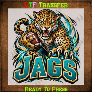 May include: A DTF TRANSFER READY TO PRESS graphic featuring a snarling leopard with blue eyes holding a brown football. The word JAGS is printed in large teal letters with gold outlines. The design includes dynamic teal and gold energy streaks.