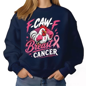May include: A navy blue crewneck sweatshirt featuring a graphic of a white rooster wearing pink boxing gloves. The text reads F-CAW-F Breast Cancer, accompanied by a pink awareness ribbon, stars, and lightning bolt accents in pink and white.