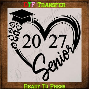 May include: A black DTF transfer design featuring a graduation cap atop a heart shape with a leopard print pattern on the left side. The numbers 2027 are centered within the heart, and the word Senior is written in a script font below.