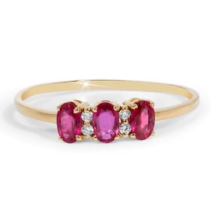 May include: A gold band ring featuring three oval-shaped ruby gemstones with smaller diamond accents.