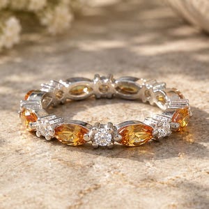 May include: A silver eternity band ring featuring alternating marquise-cut yellow citrine gemstones and round-cut clear white diamonds set in a continuous metal frame that encircles the entire circumference of the circular jewellery piece.