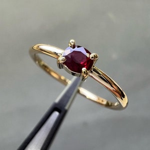 May include: A gold ring with a red ruby gemstone set in a four-prong setting.