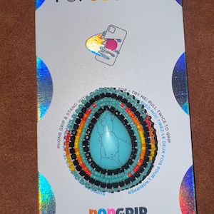 May include: A PopSockets PopGrip with a turquoise stone center, surrounded by colorful beads in a circular pattern. The packaging features the PopSockets logo and instructions.