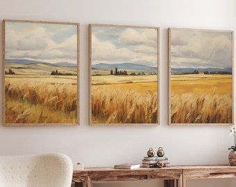 May include: Three framed landscape paintings depicting a field of golden wheat with a distant view of a small town and rolling hills. The paintings are hung on a white wall above a wooden table and a white armchair.