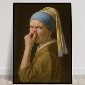 May include: A framed art print featuring a parody of Johannes Vermeer's "Girl with a Pearl Earring." The subject, wearing a blue headscarf and pearl earring, pinches her nose in disgust. The artwork is set against a dark background.
