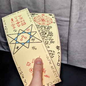 Peut inclure: Deux rouleaux de papier beige avec du texte et des symboles noirs et rouges. Les rouleaux sont enroul&eacute;s et tenus dans une main. Le texte sur les rouleaux est dans une langue &eacute;trang&egrave;re. Les rouleaux sont d&eacute;cor&eacute;s d'une &eacute;toile bleue et rouge avec un cercle au centre.