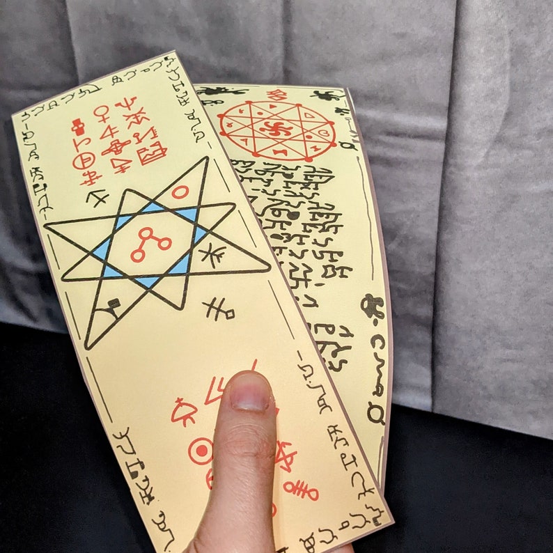 Peut inclure: Deux rouleaux de papier beige avec du texte et des symboles noirs et rouges. Les rouleaux sont enroul&eacute;s et tenus dans une main. Le texte sur les rouleaux est dans une langue &eacute;trang&egrave;re. Les rouleaux sont d&eacute;cor&eacute;s d'une &eacute;toile bleue et rouge avec un cercle au centre.
