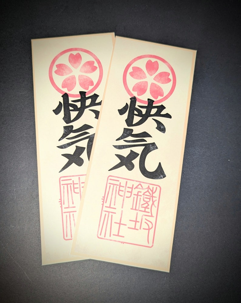 Peut inclure: Deux autocollants en papier cr&egrave;me avec un motif de cerisier rose. Les autocollants pr&eacute;sentent les caract&egrave;res japonais "桜" (sakura) et "祭" (matsuri) sur l'autocollant de gauche et "桜" (sakura) et "元" (moto) sur l'autocollant de droite. Les autocollants ont &eacute;galement un tampon rouge avec des caract&egrave;res japonais.