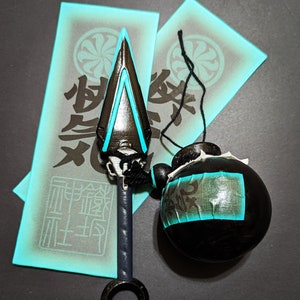 Peut inclure: Une arme de ninja noire et bleue avec une poign&eacute;e en anneau et un r&eacute;cipient rond bleu et noir avec des caract&egrave;res japonais. L'arme et le r&eacute;cipient sont sur une surface grise avec deux &eacute;tiquettes en papier turquoise avec des caract&egrave;res japonais.