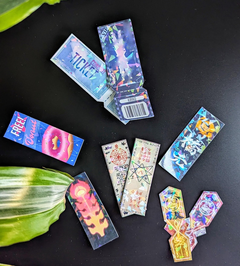 May include: A collection of holographic stickers featuring various designs, including a donut, a ticket, a star, and a flame. The stickers are iridescent and have a rainbow effect.