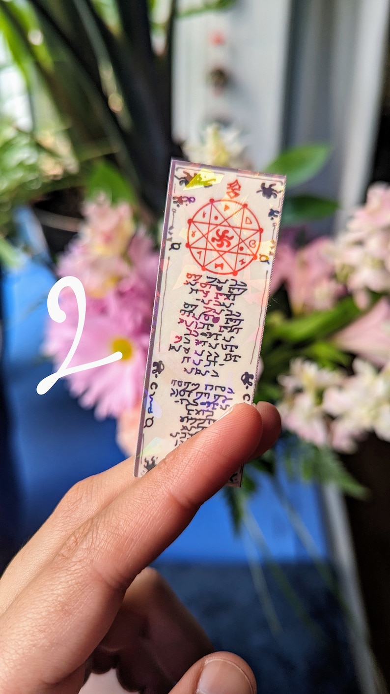 May include: A white card with a red and black symbol in the center. The card has a holographic finish and is surrounded by a black border. The card has text written in a foreign language.