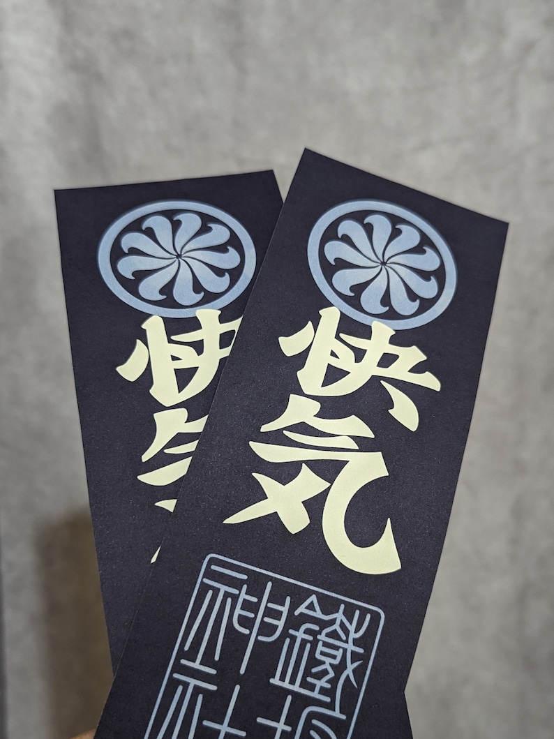 Peut inclure: Deux autocollants noirs et blancs avec un motif de fleur stylis&eacute; bleu et blanc. Les autocollants pr&eacute;sentent les caract&egrave;res japonais "忍" et "忍" en blanc. L'autocollant du bas pr&eacute;sente &eacute;galement les caract&egrave;res japonais "耐え忍ぶ" en noir.