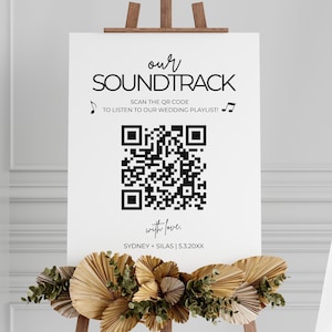 Könnte beinhalten: Ein weißes Schild mit schwarzem Text, der "our SOUNDTRACK SCAN THE QR CODE TO LISTEN TO OUR WEDDING PLAYLIST!" lautet, mit einem schwarzen QR-Code in der Mitte. Unter dem QR-Code befindet sich der Text "with love. SYDNEY + SILAS | 5.3.20XX"