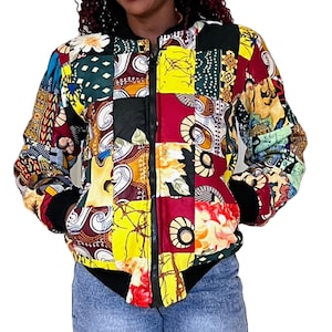 May include: A colorful patchwork bomber jacket with a zipper closure. The jacket is made of different fabrics with various patterns, including floral, geometric, and abstract designs. The colors are vibrant and include red, yellow, green, blue, and black.