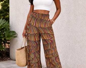 Könnte beinhalten: Eine Frau trägt ein weißes Tanktop und eine gemusterte Palazzo-Hose. Die Hose hat ein mehrschichtiges Design mit einem sich wiederholenden Muster aus roten, gelben und braunen Punkten. Sie trägt auch eine gewebte Stroh-Tragetasche.