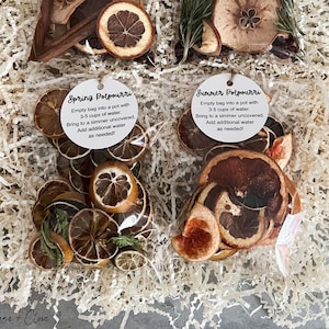May include: Four clear bags of potpourri, each labeled for a different season: Fall, Winter, Spring, and Summer. Each bag contains dried fruits and botanicals. Instructions are included on each tag: "Empty bag into a pot with 3-5 cups of water."