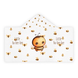 May include: White hooded towel with a cute cartoon bee illustration and the text "little ha-bee-bee". The towel is covered in a pattern of small yellow bees.