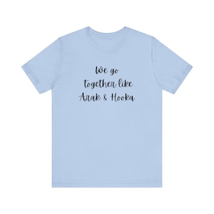 May include: Light blue t-shirt with the text "We go together like Arak & Hooka" in black script. The shirt is a solid color and has short sleeves and a crew neck.
