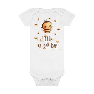 Op de afbeelding: Witte baby romper met een cartoon-bij en de tekst "Little ha-bee-bee".