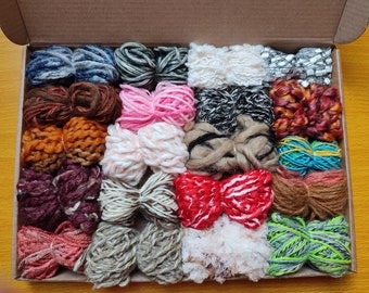 May include: A box filled with a variety of colorful yarn skeins. The yarn is in different textures and colors, including red, white, blue, green, brown, and orange.
