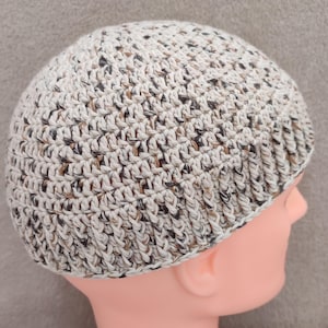 Puede incluir: Un gorro de punto de ganchillo con un patrón moteado marrón y blanco. El gorro está hecho con un hilo suave y tiene un diseño simple y clásico.
