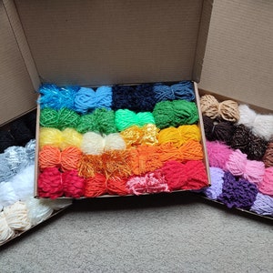 Pode incluir: Três caixas de cartão cheias de novelos de lã coloridos. A lã é de diferentes texturas e cores, incluindo azul, verde, vermelho, laranja, amarelo, branco e castanho.