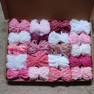 May include: A box filled with various shades of pink, white, and red yarn. The yarn is arranged in rows and is ready for crafting projects.
