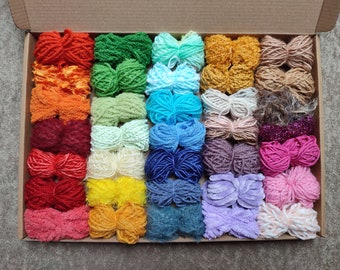 May include: A collection of 24 colorful yarn skeins in a cardboard box. The yarn is arranged in rows of different colors, including red, orange, yellow, green, blue, purple, and pink.