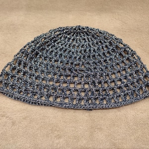 May include: A blue and silver crocheted beanie hat. The hat is made with a loose, open weave, creating a net-like appearance. The color is a mix of dark blue and silver threads, giving it a shimmering effect. The hat is round and has a simple, classic design.