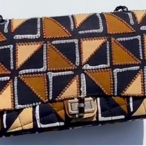 May include: A rectangular shoulder bag featuring a geometric pattern of black, tan, and brown triangles. The edges of the shapes are outlined with small, reflective silver and gold-toned beads. It includes a silver-toned metal turn-lock closure.