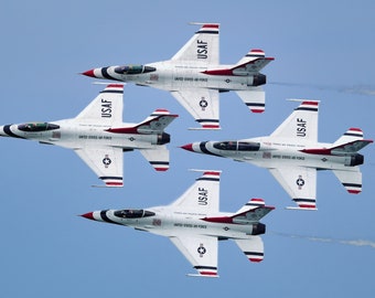 Puede incluir: Cuatro aviones de combate blancos de la USAF en formación contra un cielo azul. Cada avión tiene detalles rojos y negros. Las palabras "UNITED STATES AIR FORCE" son visibles en el fuselaje.