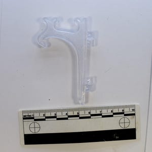 May include: A transparent plastic display stand with a curved top and a vertical support. The stand has two small hinges on the side. A ruler with metric measurements is below the stand.