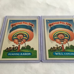 May include: Two Cabbage Patch Kids trading cards featuring illustrations of a boy inflating with an air pump. The card on the left says "Pumping Aaron" and the card on the right says "Will Explode".