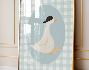 May include: Framed art print featuring a cartoon goose wearing a black cap, set against a light blue oval. The background is a light blue and white checkered pattern. The artwork is framed in a gold-colored frame.