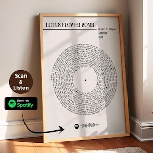 May include: A framed print of a black and white record with the title "LOTUS FLOWER BOMB" by WALE ft. Migos. The record is surrounded by lyrics from the song. The print is hanging on a wall in a room with a wooden floor and a plant on a table.