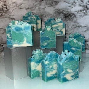 May include: A collection of handmade soap bars with a swirling blue and white design. The bars are arranged on a gray surface.