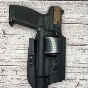 May include: A black polymer holster with a black metal clip for a handgun. The holster has a textured surface and is designed to be worn on a belt.