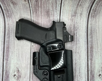 Puede incluir: Pistola negra con una mira de punto rojo en una funda negra. La funda tiene un clip para cinturón y un ángulo ajustable.