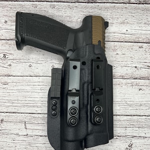 May include: A black handgun holster with a black gun inside. The holster has two adjustable clips and a black polymer construction.