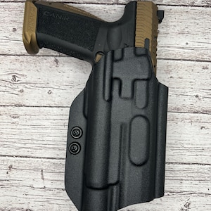 May include: A black leather holster with a brown and black handgun inside. The holster has two black screws on the side.