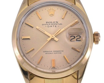 May include: A gold Rolex Oyster Perpetual Date wristwatch with a champagne-colored dial, black hands, and a date window at the 3 o'clock position. The watch has a gold bracelet and a gold case.
