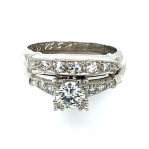 May include: A platinum engagement ring set with a round brilliant cut diamond center stone and a matching band with smaller diamonds.