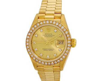 May include: A gold Rolex Oyster Perpetual Datejust watch with a diamond bezel and a gold bracelet. The watch face is gold with black Roman numeral hour markers and a date window at the 3 o'clock position. The watch face also features the text "Rolex Oyster Perpetual Datejust" and "Superlative Chronometer Officially Certified".