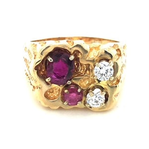 Puede incluir: Un anillo de oro con una banda texturizada y tres piedras preciosas. Dos de las piedras preciosas son redondas y rojas, y una es redonda y clara.