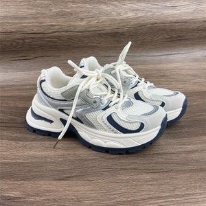May include: White and silver trainers with a chunky platform sole and blue accents. The laces are white and the shoes have a mesh upper.