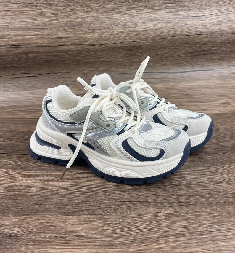 May include: White and silver trainers with a chunky platform sole and blue accents. The laces are white and the shoes have a mesh upper.