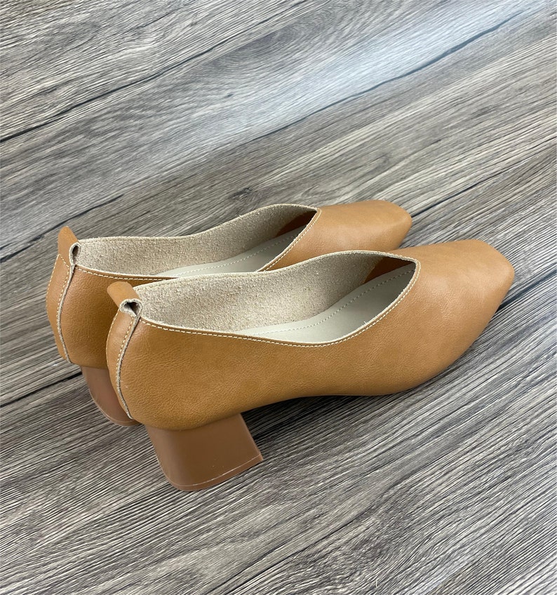 May include: A pair of brown leather heeled shoes with a square toe. The shoes have a block heel and a white lining.