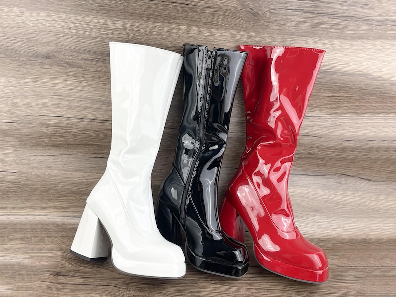 K&ouml;nnte beinhalten: Drei Paar kniehohe Stiefel in Wei&szlig;, Schwarz und Rot. Die Stiefel haben einen Plateauabsatz und eine spitze Zehenpartie.