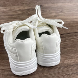 May include: A pair of white leather sneakers with white laces. The sneakers have a thick white sole and a rounded toe.